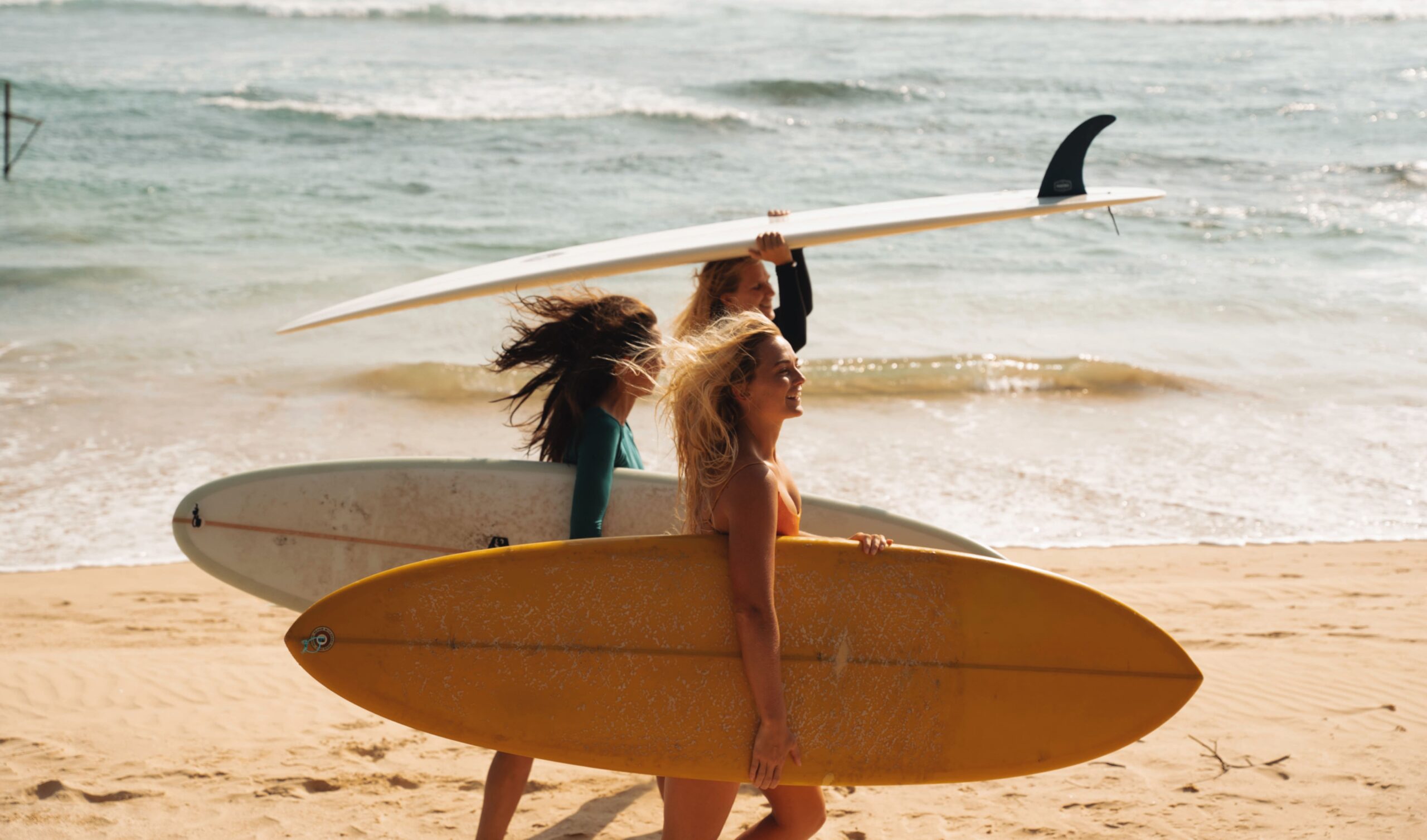 Ride The Board -Ride The Board Girls walking on the beach with surfboard scaled